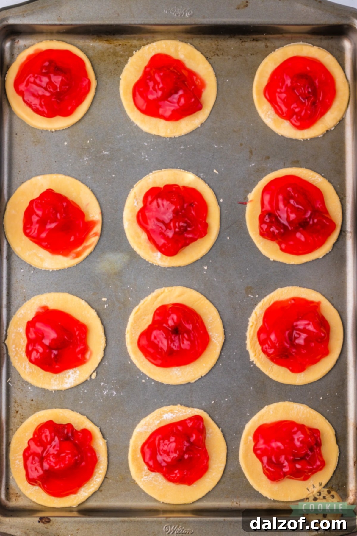 Strawberry pie filling being carefully spooned onto the center of cut pie crust circles, ready for the next step in creating mini strawberry pies.