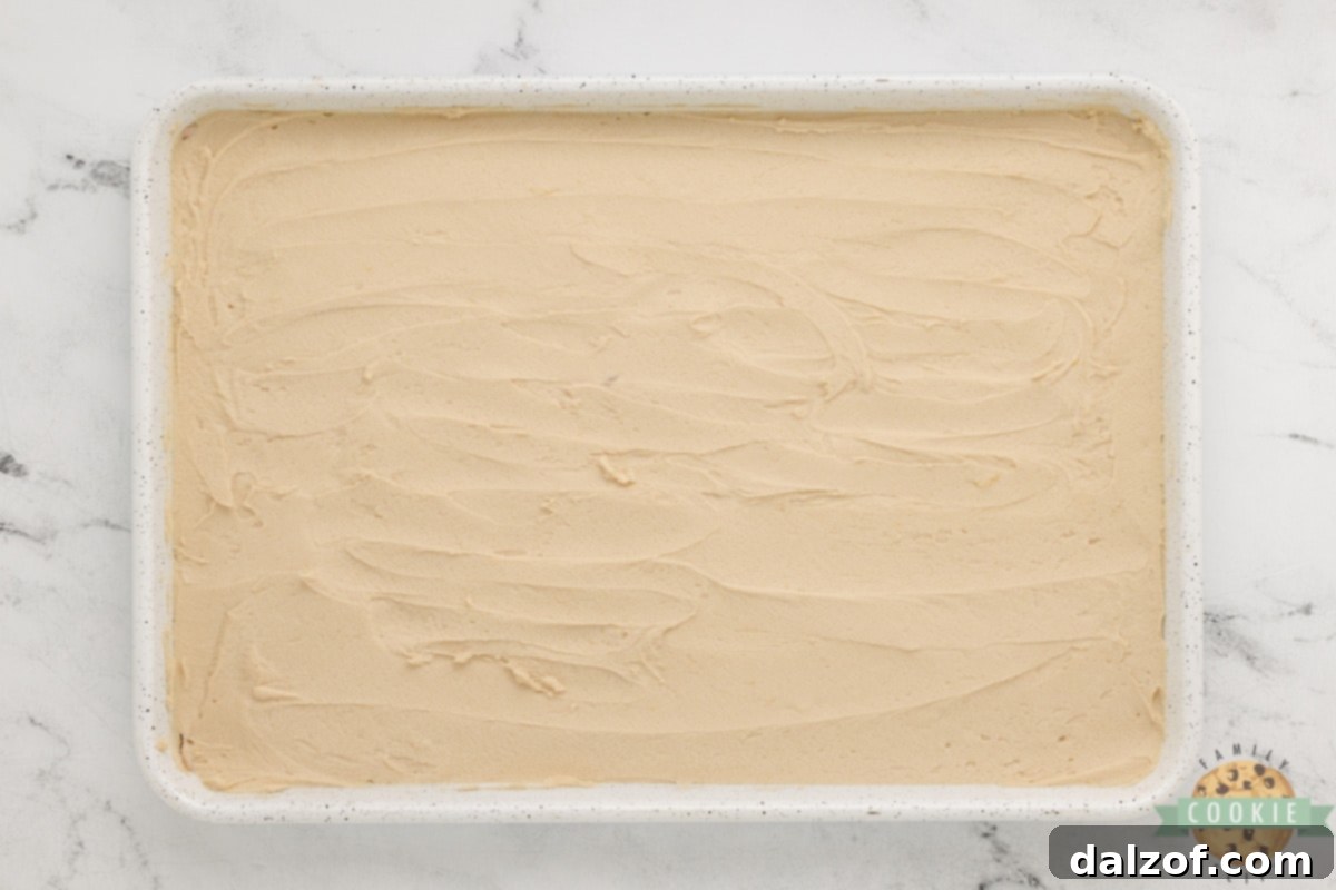 Spreading the thick Snickerdoodle cookie dough evenly into a prepared baking pan with a knife, ensuring it reaches all edges.