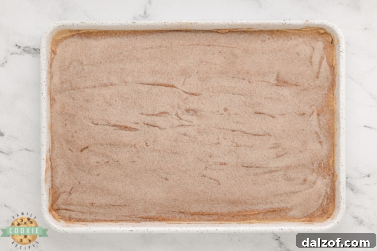 A baking pan filled with Snickerdoodle cookie dough, generously topped with a mixture of cinnamon and sugar, ready for baking.