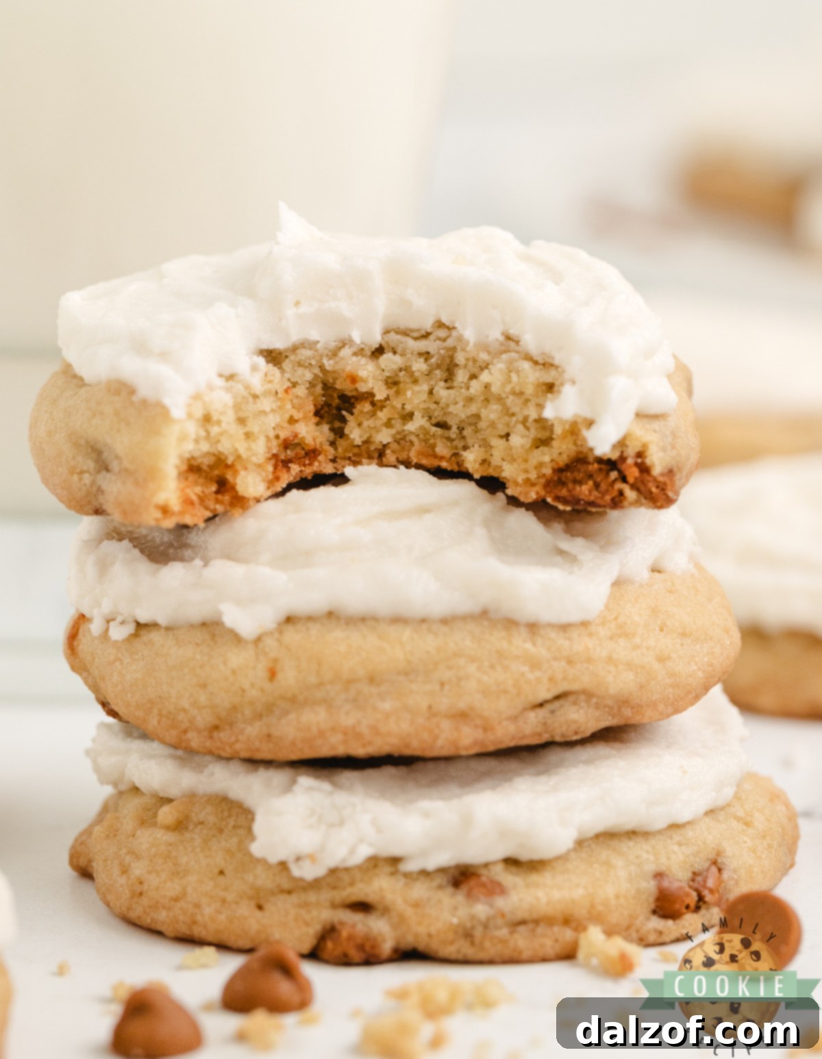A stack of three Iced Cinnamon Chip Cookies on a white plate, showcasing their soft texture, visible cinnamon chips, and thick vanilla frosting. The background is blurred, focusing on the delicious treats.