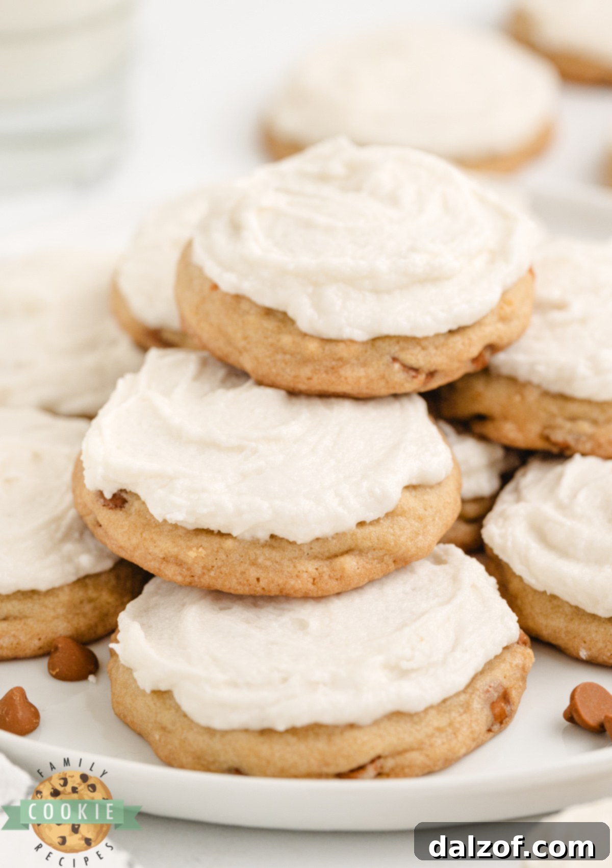 A single Iced Cinnamon Chip Cookie, exquisitely frosted with creamy vanilla icing, sits on a pristine white surface, highlighting its perfect shape and appetizing appearance.