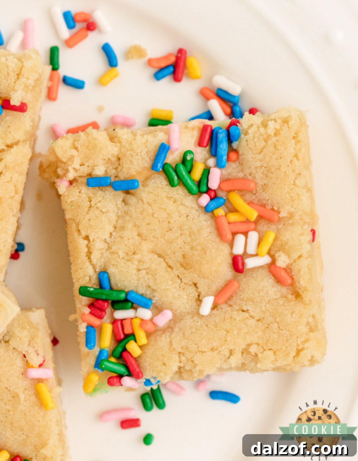 Sugar cookie bars with a cheesecake filling and sprinkles, arranged on a serving plate.