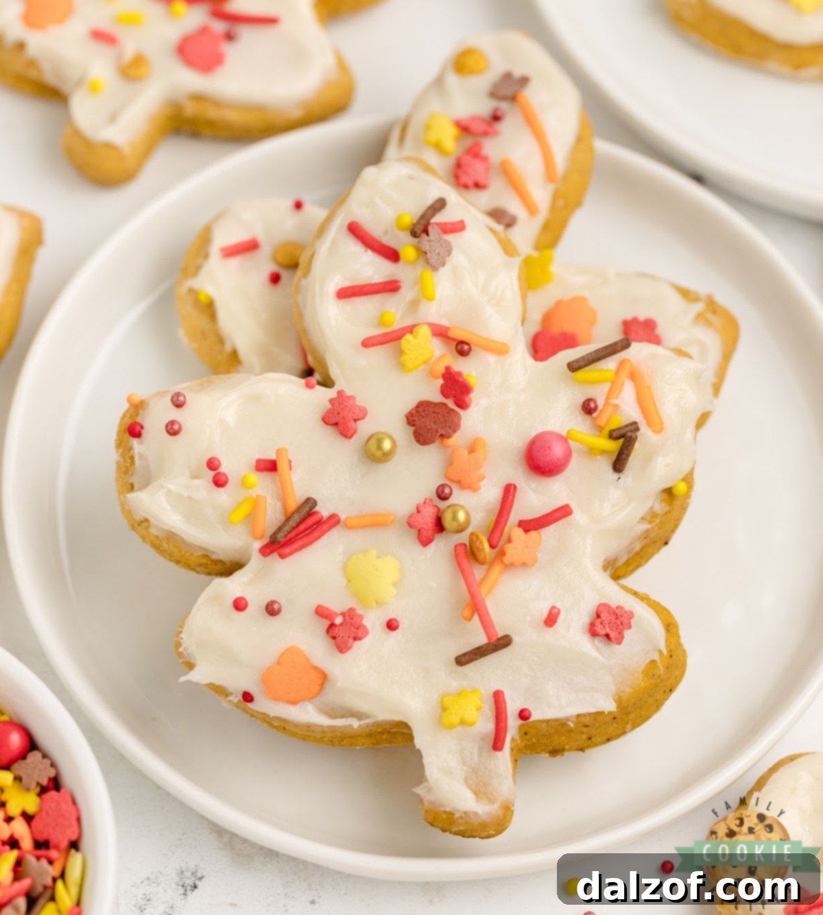 Close-up of frosted Pumpkin Sugar Cookies with cream cheese frosting and sprinkles.