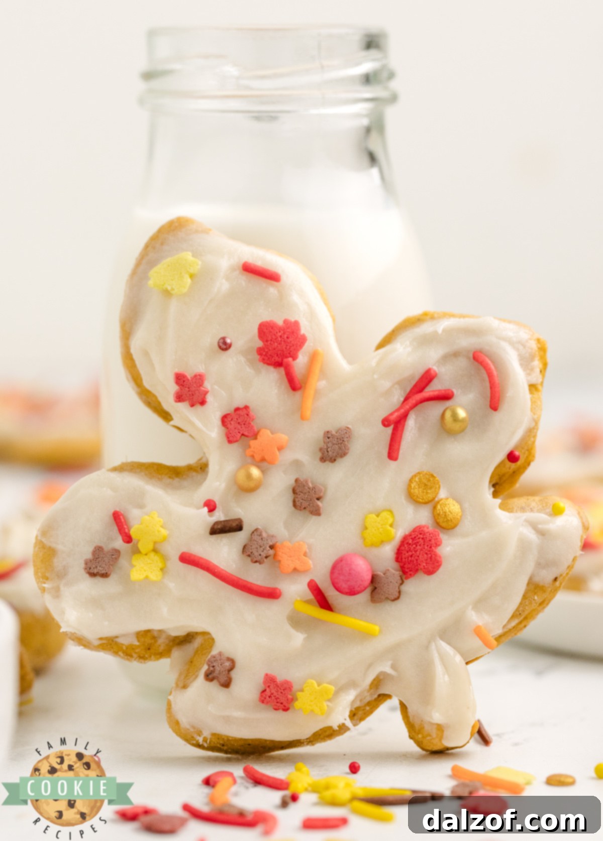 A decorated Pumpkin Sugar Cookie with a glass of milk.