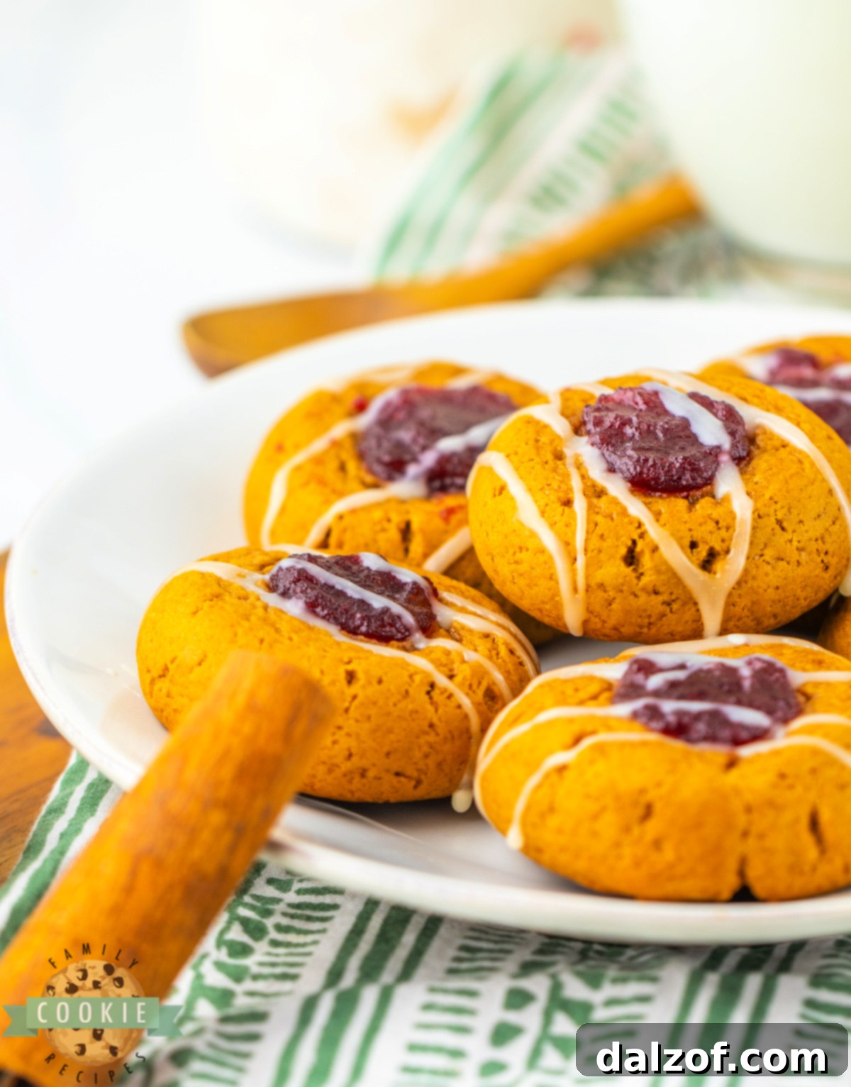 A hand drizzling melted white chocolate over a tray of Gingerbread Thumbprint Cookies with Cranberry Sauce.