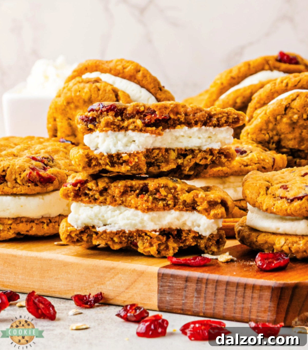 Soft pumpkin oatmeal cookies with dried cranberries and creamy frosting filling stacked on a wooden cutting board.