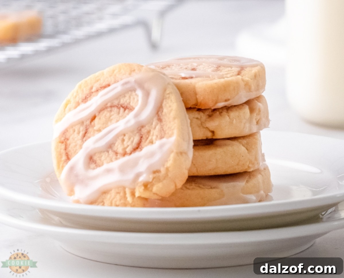 Freshly baked cinnamon roll cookies drizzled with white icing on a white plate, showcasing their inviting golden-brown color and sweet swirl.