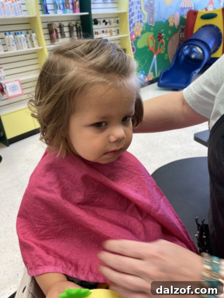 A cute two-year-old girl with a new short haircut, smiling for the camera.