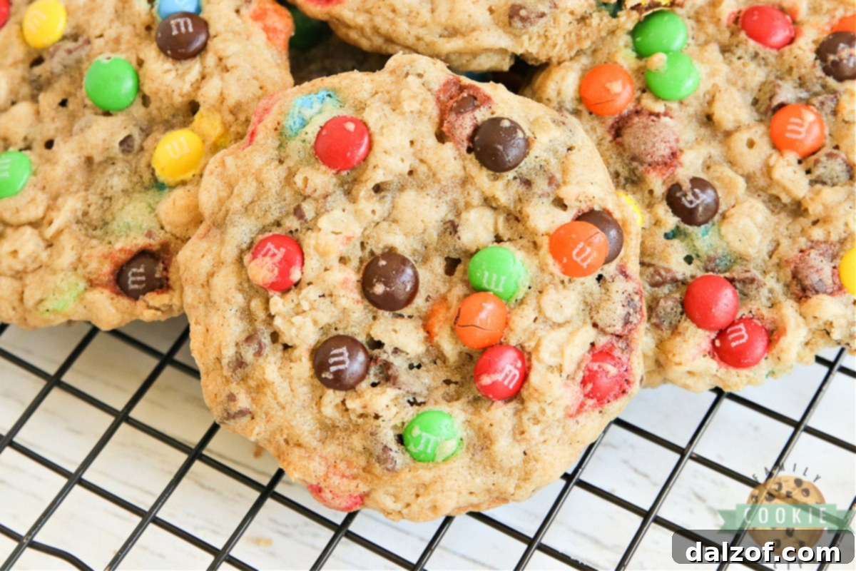 A stack of M&M Oatmeal Cookies on a white plate, with a bowl of M&Ms in the background, highlighting the cookies' texture.