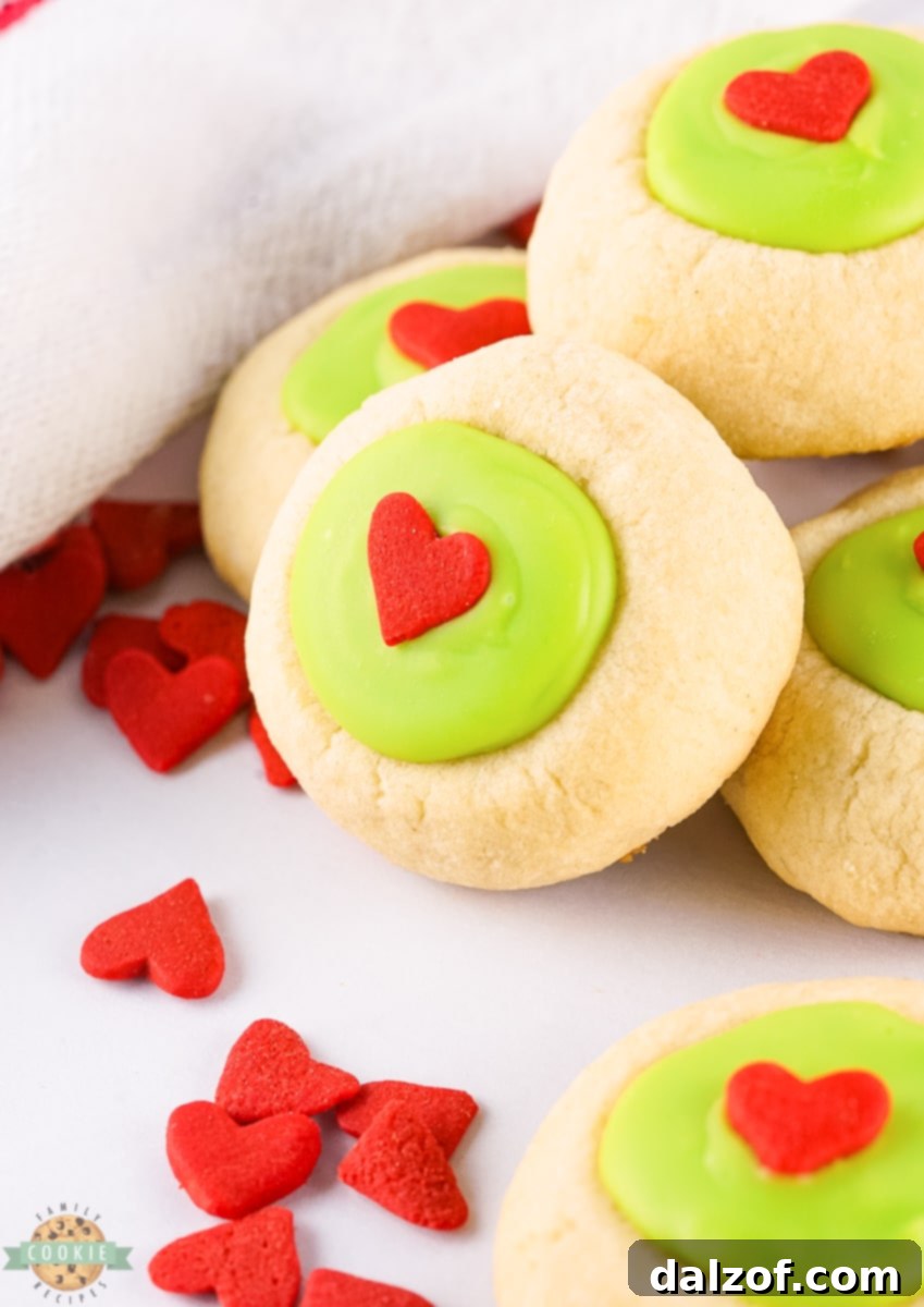 Close-up of finished Grinch Thumbprint Cookies with green filling and red heart sprinkles.