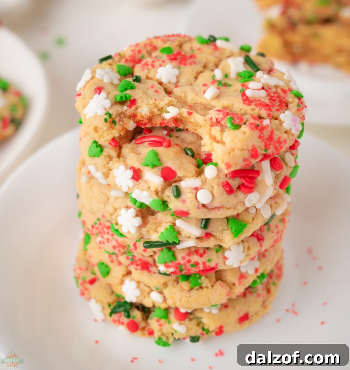 A stack of golden-brown Christmas sprinkle cookies, adorned with colorful sprinkles, on a festive backdrop.