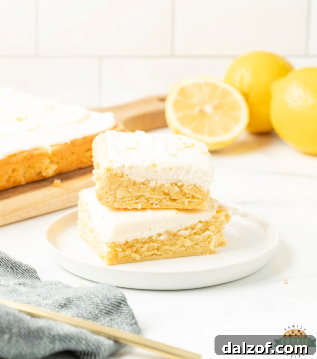 Lemon cookie bars cut into squares and topped with cream cheese frosting and fresh lemon zest on a white plate.