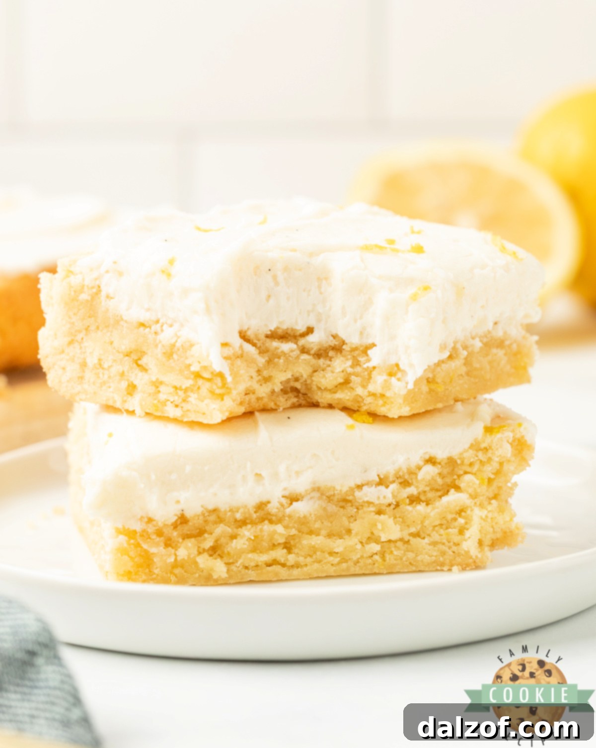 Stack of two lemon cookie bars with cream cheese frosting.