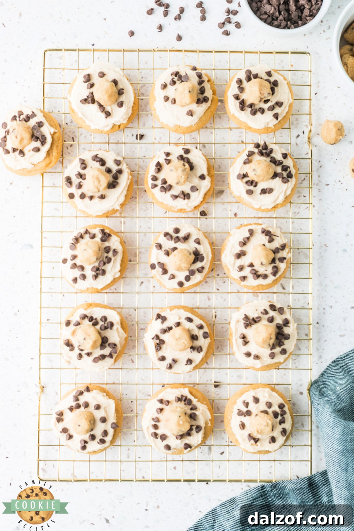 Cookie dough frosted cookies topped with edible cookie dough pieces and mini chocolate chips on a wire rack. 