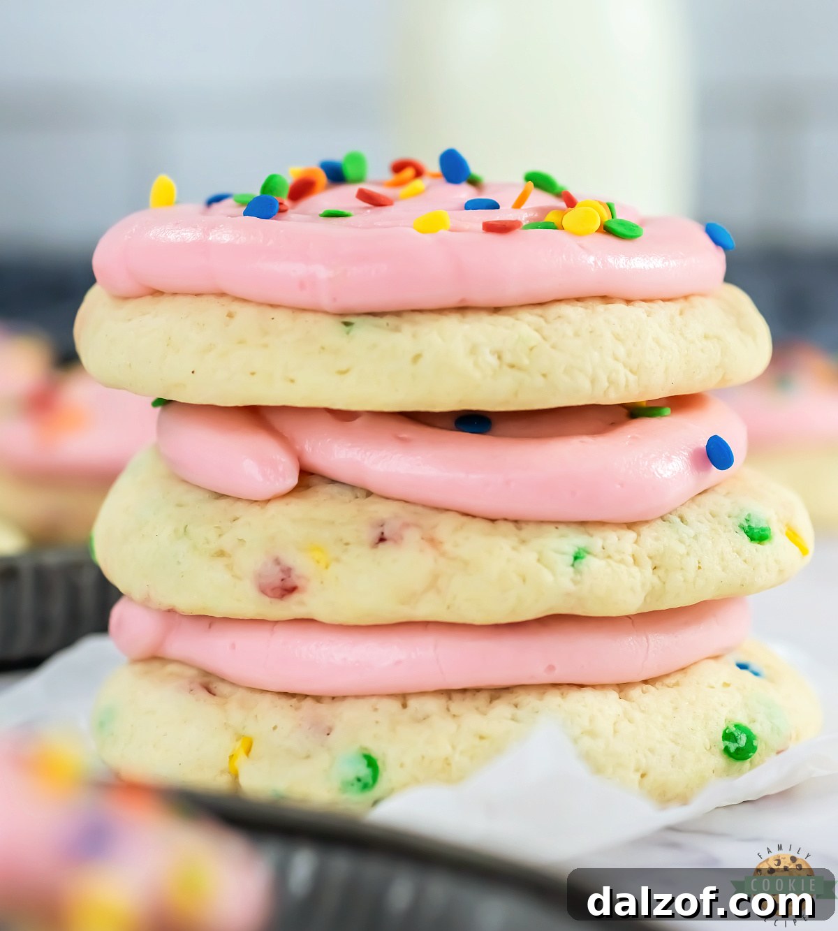 A stack of copycat Crumbl confetti cake cookies with pink frosting and sprinkles, showing the soft thick texture