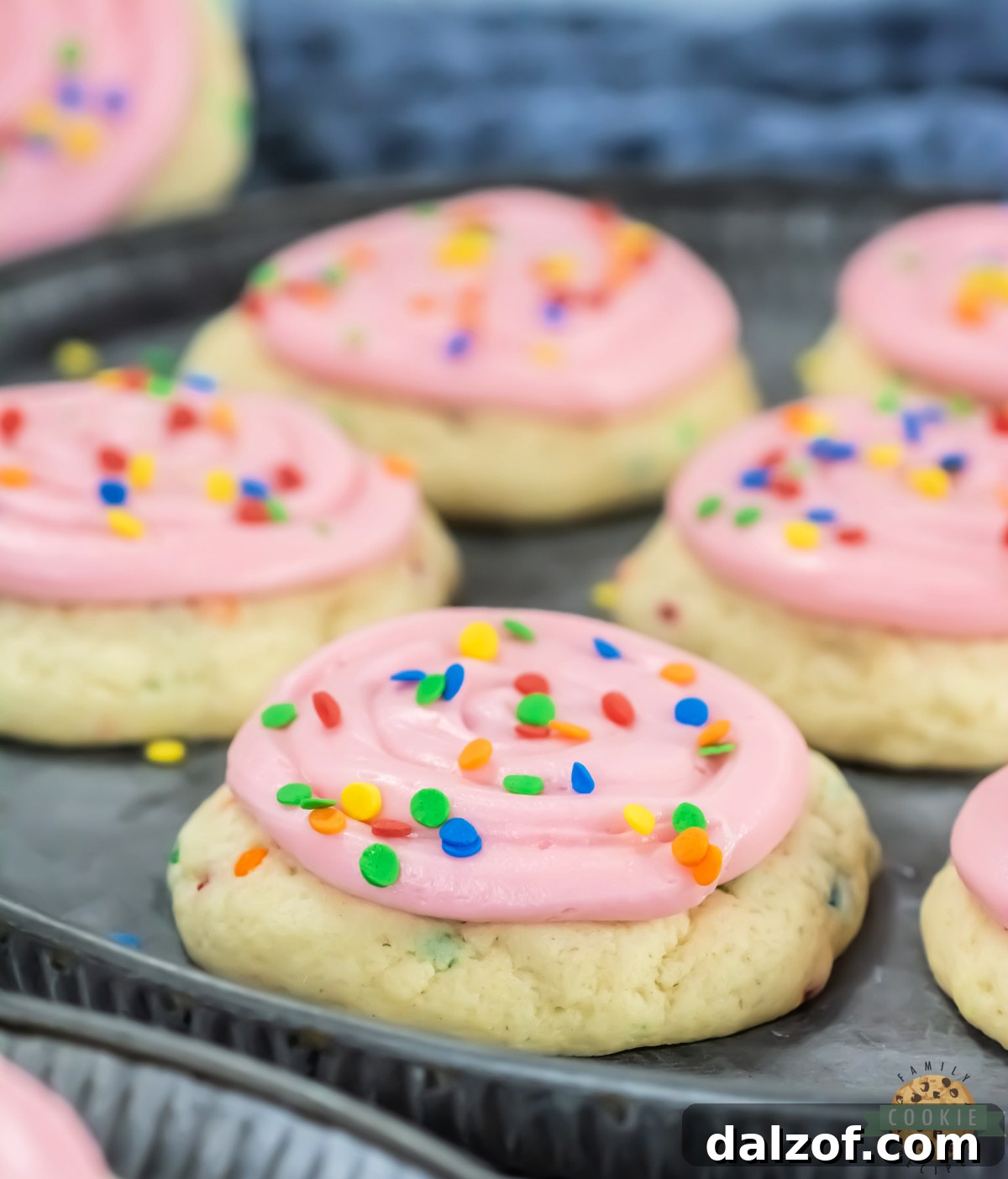 A single thick copycat Crumbl confetti cake cookie with a swirl of pink cream cheese frosting and sequin sprinkles on top
