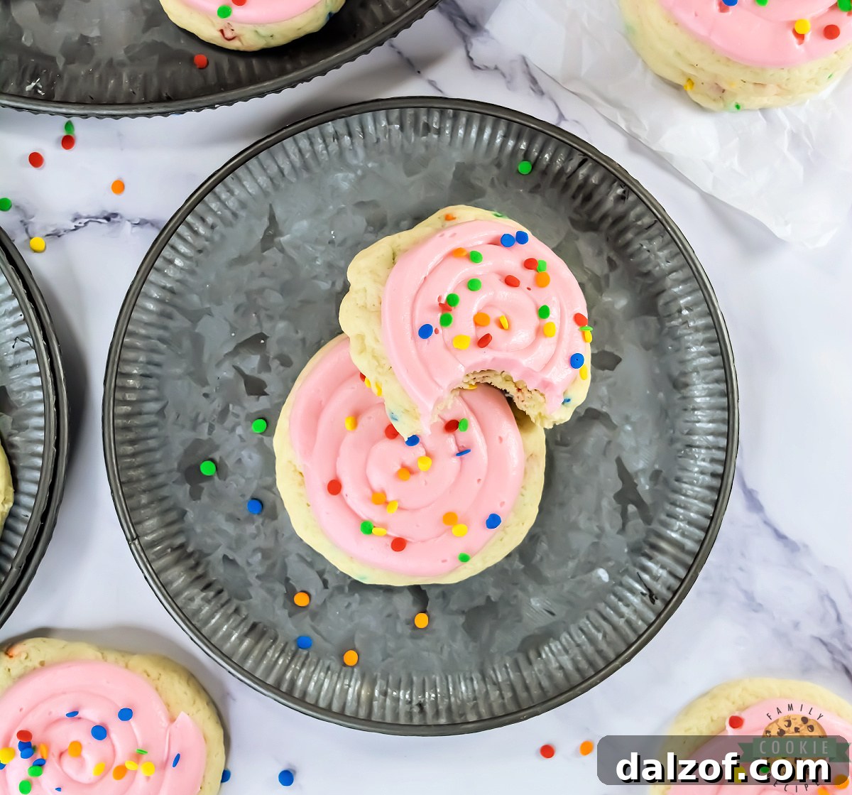 A plate of Crumbl copycat confetti cake cookies with pink frosting and sequin sprinkles, ready to serve