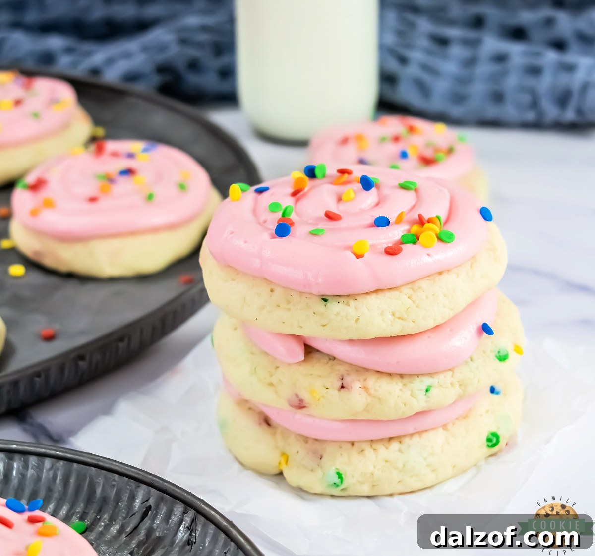 A stack of copycat Crumbl confetti cake cookies with pink frosting and sprinkles, showing the soft thick texture