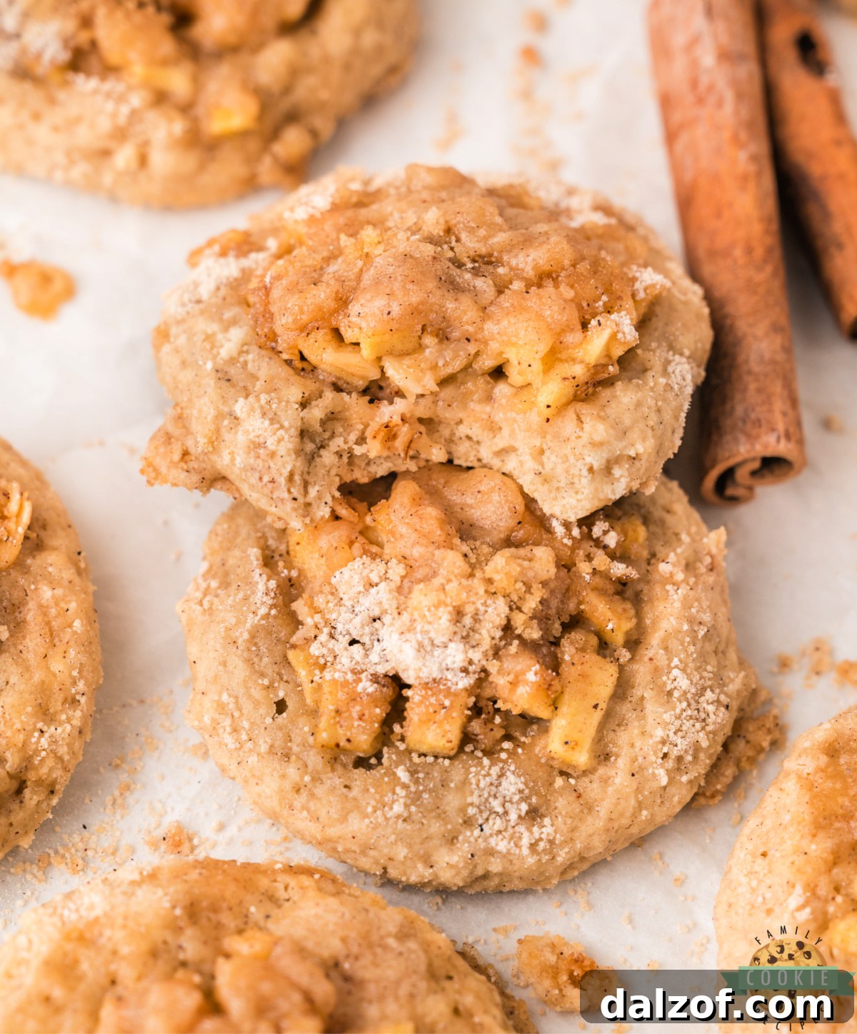 Apple crisp cookies on parchment paper showing the juicy apple filling, crisp oat topping, and icing drizzle on top of soft cinnamon cookies