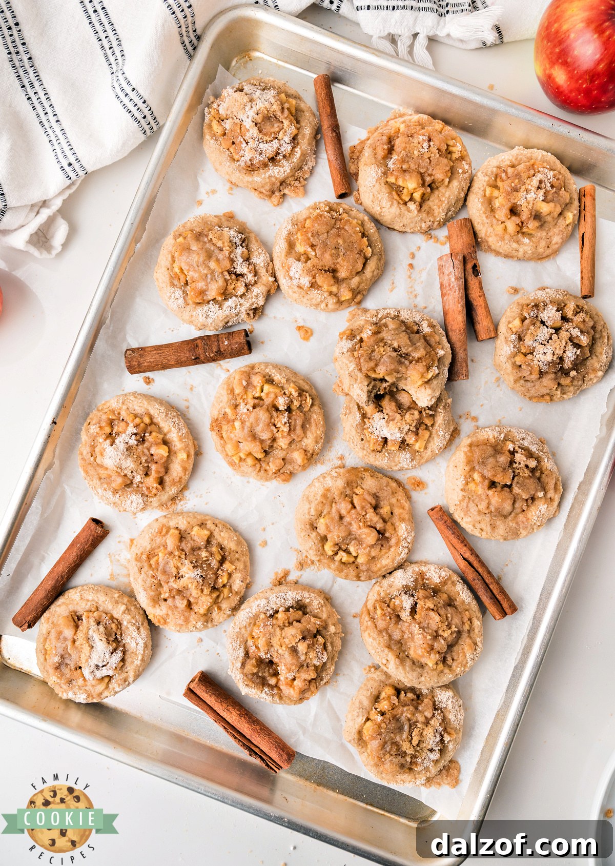 Apple crisp cookies on a cookie sheet lined with parchment paper showing the juicy apple filling, crisp oat topping, and icing drizzle on top of soft cinnamon cookies